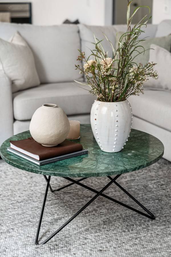 A green marble coffee table with white vases, books and fresh stems