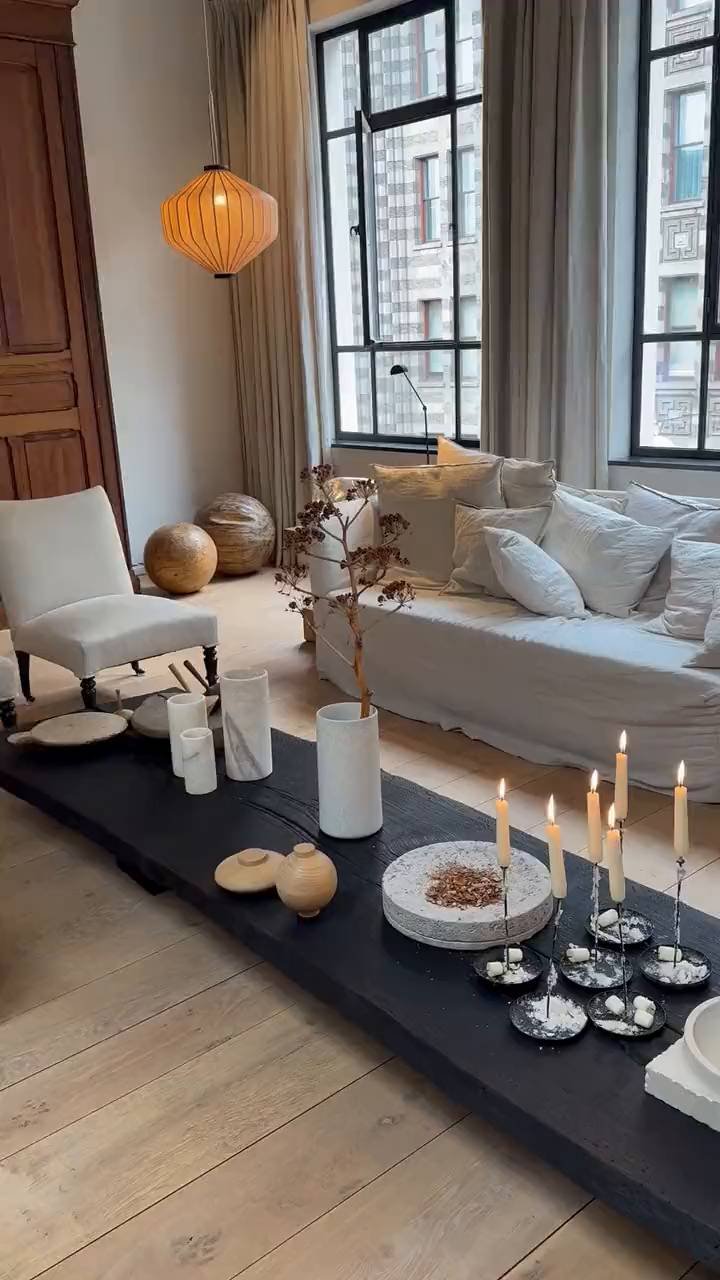 A modern-classic loft living room: a deep linen sofa, steel-framed windows and a low black table set with candlesticks
