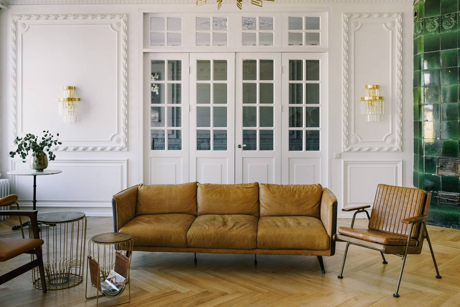 A modern-classic living room: moulded white walls, glazed doors, a cognac leather sofa and herringbone floors