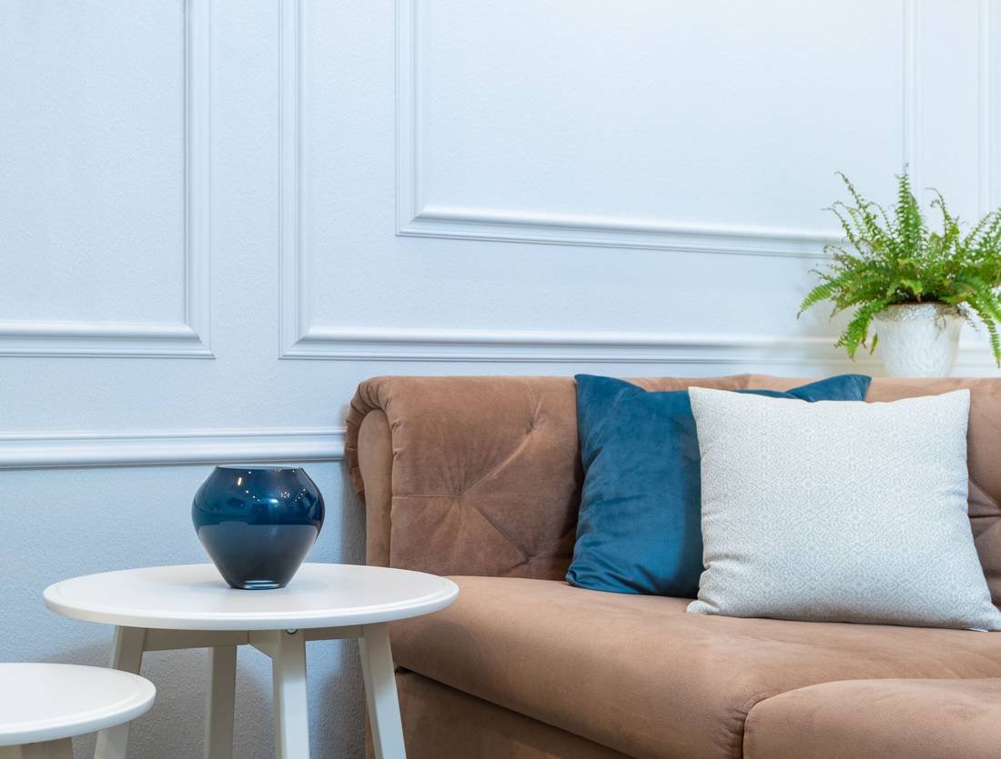 A bright living room with white wall panelling, a blush sofa, blue cushions and a fern