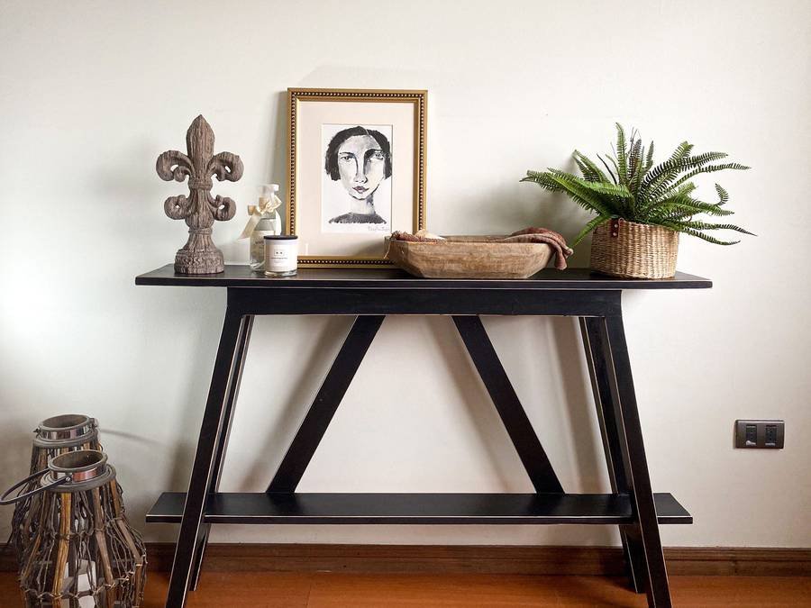 A black console table styled with a portrait sketch, a fern and a woven tray
