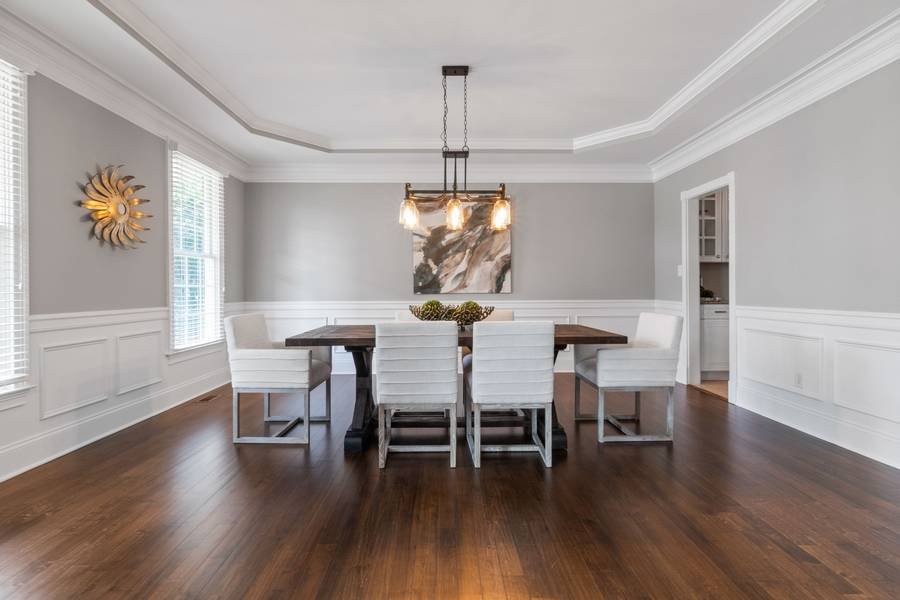 A dining room with white wainscoting, a long table and a sculptural pendant over dark wood floors